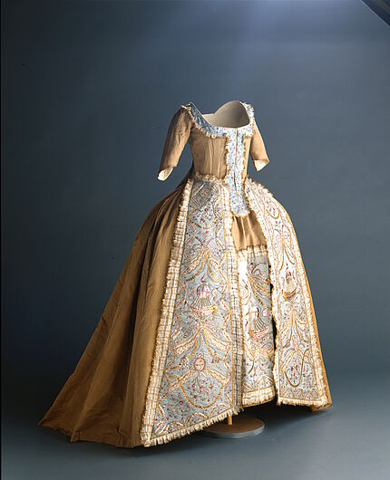 Robe à la française mit Ballonmotiven Robe à la française, 18. Jahrhundert, Seitenansicht: goldbeiges Oberkleid mit Schleppe, hellblauer Unterrock mit pinkfarbenen Heißluftballon-Stickereien, weit ausgestellte Reifrock-Silhouette.