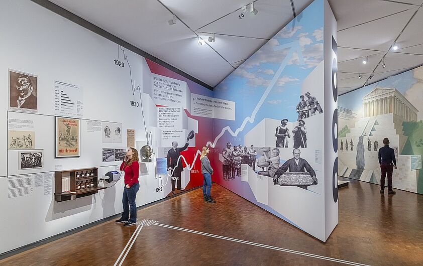 Menschen betrachten aufmerksam eine Ausstellung im Museum, die mit Bildern und Postern gestaltet ist.