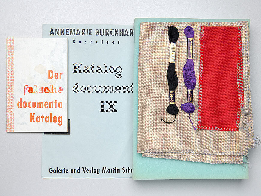 Flach ausgelegt sind neben dem "falschen Katalog für die documenta 9“, eine Broschüre und das Bastelset bestehend aus verschiedenen Garnen und Stoffen zur documenta 9 zu sehen.
