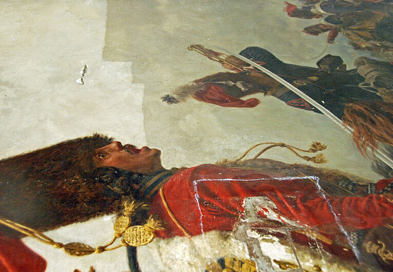 Restaurierung eines großformatigen Leinwandgemäldes. Vorn im Bild ist ein alter Riss erkennbar. Hier ist das Gemälde während der Oberflächenreinigung zu sehen. Im oberen Bildteil wird der schon gereinigte Bereich sichtbar.