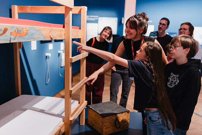 Eine Gruppe mit Kindern und Erwachsenen stehen vor einem Museumsobjekt