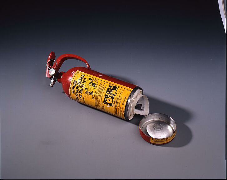 Ein unter geöffneter Feuerlöscher mit Zeitungen darin.