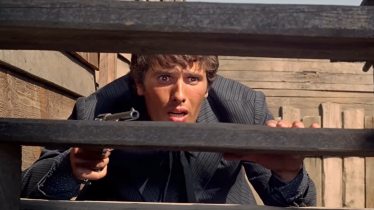 Ein Mann hat eine Waffe in der Hand, beugt sich und versteckt sich hinter einem Zaun.