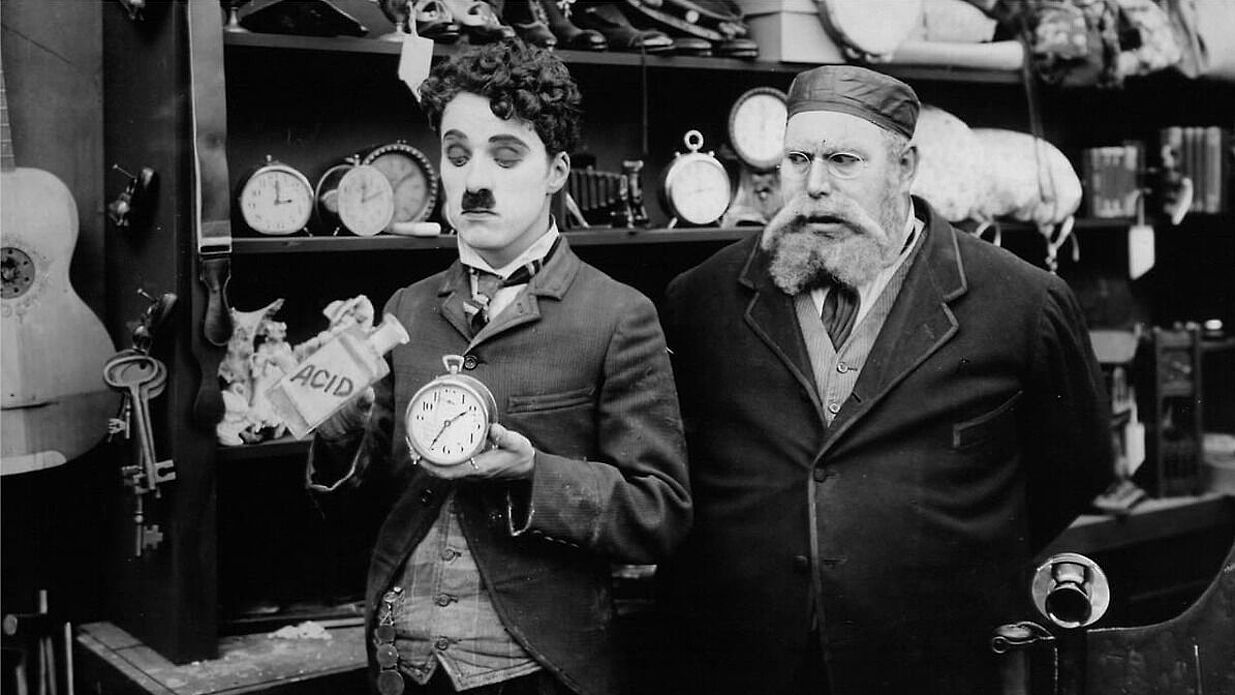 Ein Mann steht neben Charlie Chaplin und blickt ihn an.