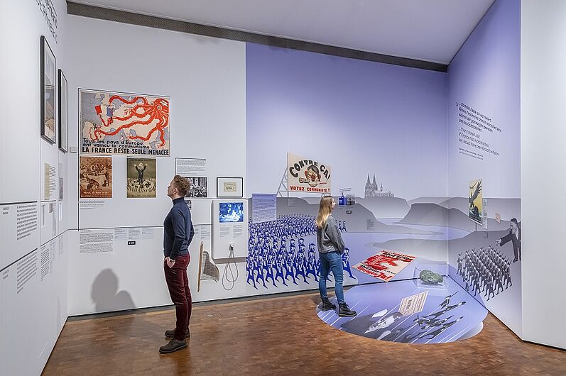 Besucher betrachten Ausstellungsstücke und Wandbilder in einem modernen Museum.