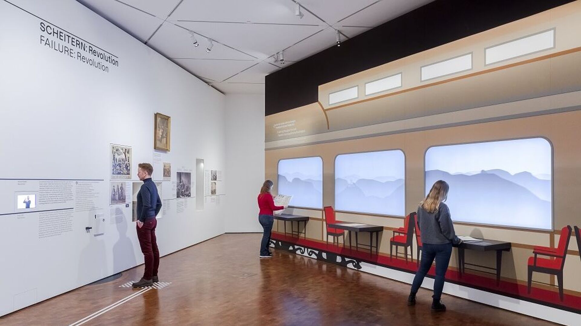 Besucher betrachten eine Museumsausstellung mit einem Wandbild von einem historischen Zug.