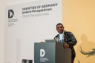 Person steht an einem Rednerpult mit Logo des Deutschen Historischen Museums, im Hintergrund Schriftzug 