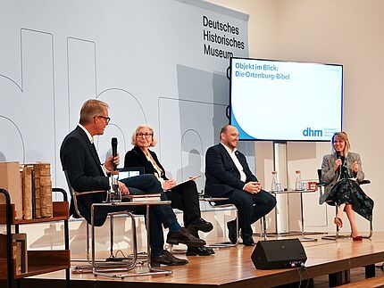 Vier Personen sitzen auf einer Bühne und sprechen miteinander.