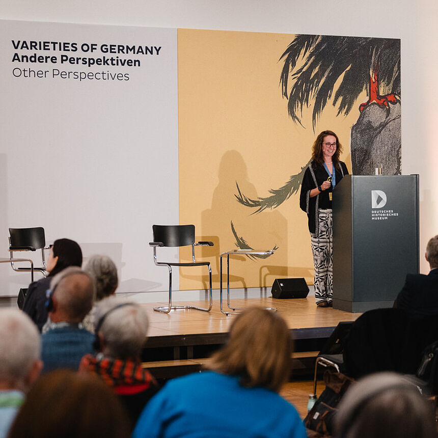 Eine Frau steht auf einer Bühne und spricht an einem Pult zum Publikum.