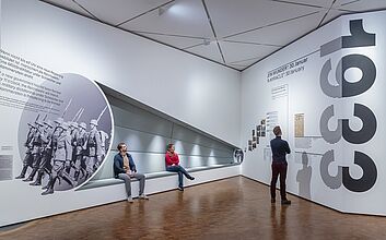 Eine Gruppe von Personen schaut auf eine umfangreiche Präsentation historischer Informationen und zeigt Interesse an den Details.