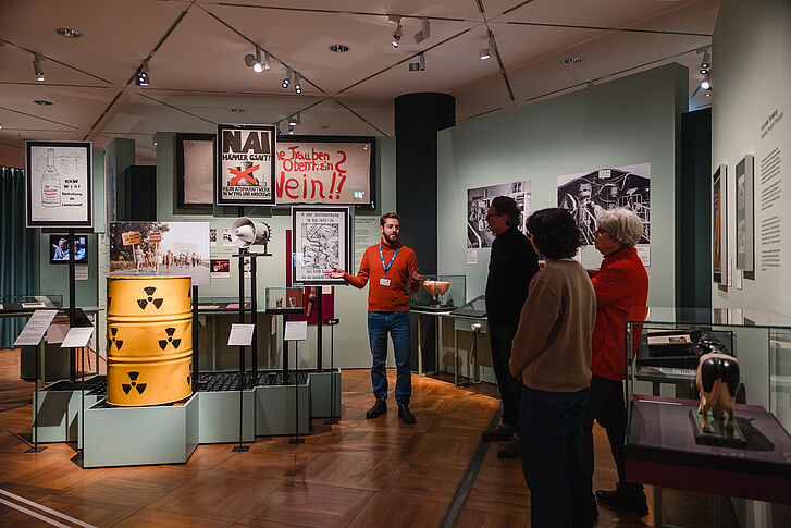 Exhibition view "Nature and German History. Faith – Biology – Power" A guide in a red sweater gives three people a tour.