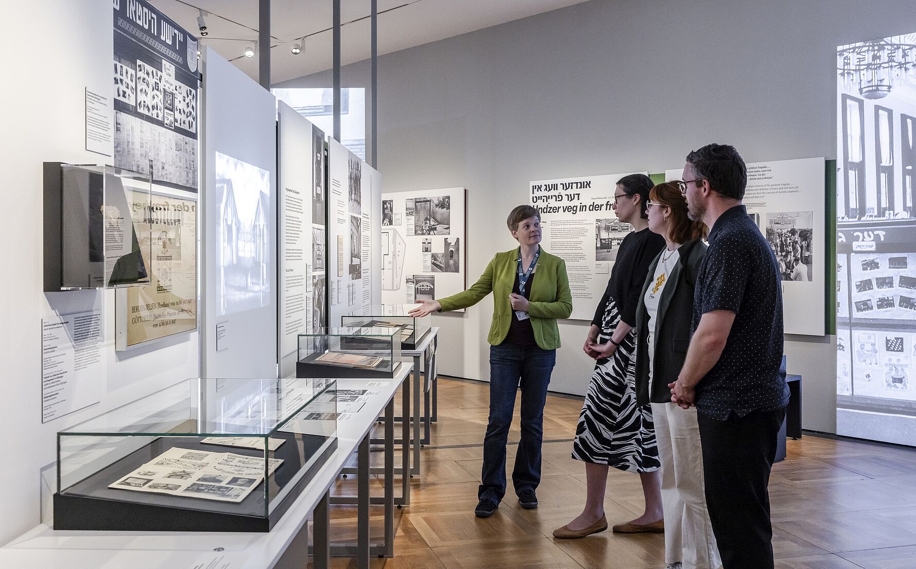 Ausstellungsansicht „Gewalt ausstellen: Erste Ausstellungen zur NS-Besatzung in Europa, 1945-1948“  Situation einer Führung in Ausstellung „Gewalt ausstellen: Erste Ausstellungen zur NS-Besatzung in Europa, 1945-1948“ mit einer weiblichen Person als Guide und drei Teilnehmenden