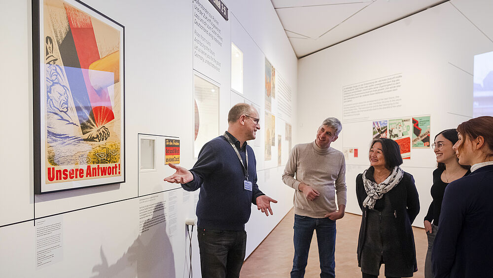 Ein Mann gibt eine Führung und steht vor einer Ausstellungswand.