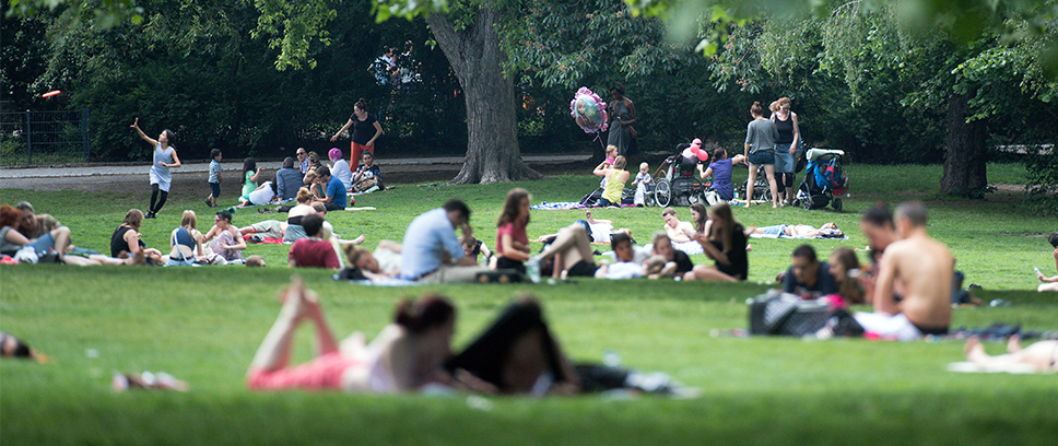 Auf dem Foto ist ein Park zu sehen. In dem park befinden sich viele Menschen, die sitzen, stehen oder rumlaufen.