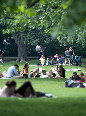 Auf dem Foto ist ein Park zu sehen. In dem park befinden sich viele Menschen, die sitzen, stehen oder rumlaufen.