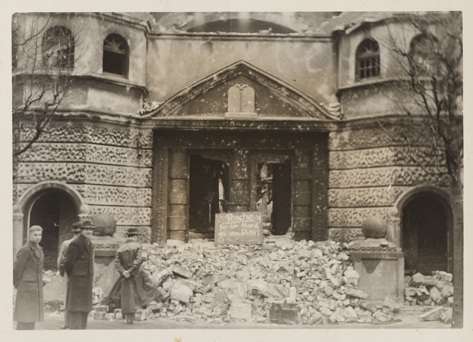 Foto: Synagoge von Wilhelmshaven nach der Pogromnacht, auf den Trümmern vor dem Eingang ein handgeschriebenes Schild: "Rache für den Mord an vom Rath", 1938