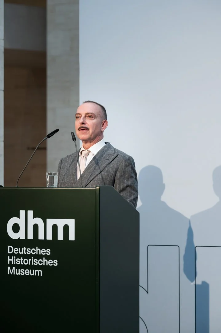 Wolfgang Cortjaens, Kurator der Ausstellung „Objekte. Geschichte. Geschichten“, steht am Rednerpult und gibt eine Einführung in die Ausstellung