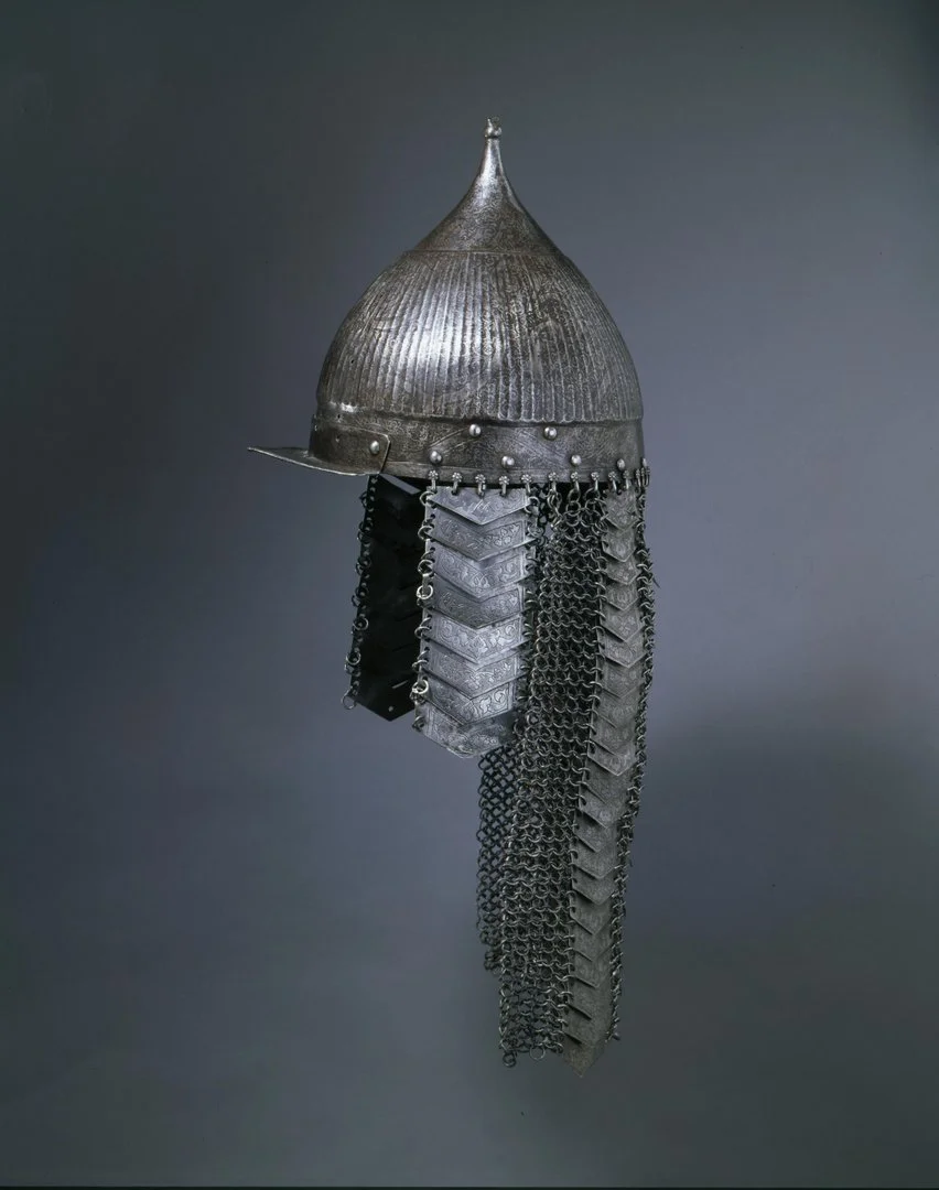 Das Bild zeigt einen Turbanhelm im osmanischen Stil. Der Helm ist aus Metall gefertigt und besteht aus einer Helmglocke mit Augenschirm sowie angebrachtem Wangen- und Schultergehänge.