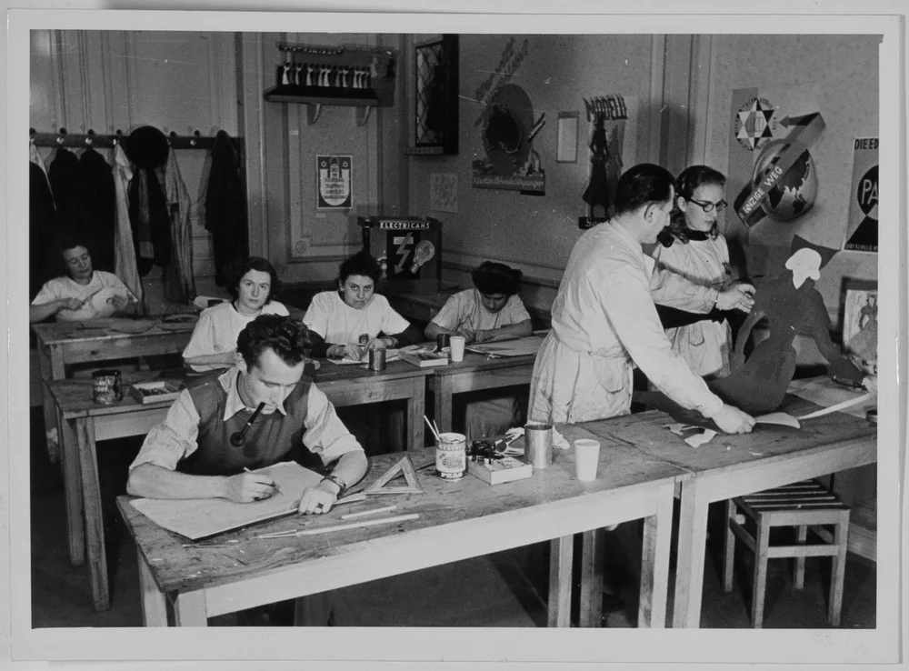 Black-and-white photograph. The picture shows Walter Preisser at a workbench in a classroom. Seven other people can be seen in the photograph.