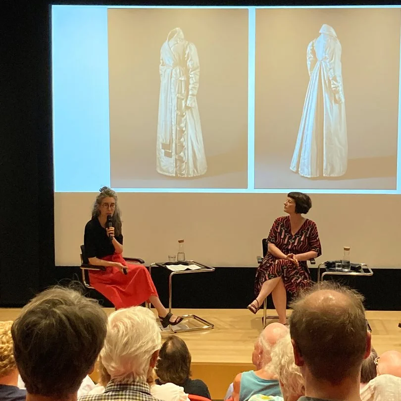 Das Foto zeigt Julia Franke und Birte Förster auf dem Podium, im Hintergrund ist die Projektion des Morgenrocks der Königin Luise zu sehen.