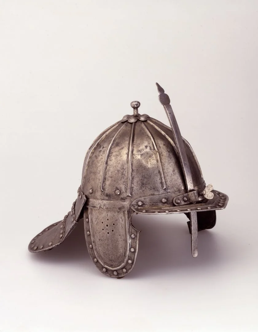 Auf dem Foto ist eine Zischägge abgebildet. Es handelt sich dabei um einen metallenen Helm mit Ohren- und Nackenblenden mit Randverzierungen.