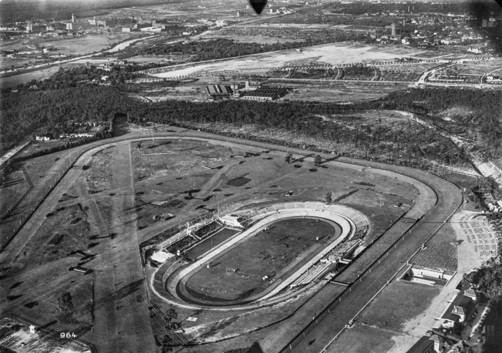 Schwarz-Weiß-Luftaufnahme eines großen Sportgeländes mit umliegender Pferderennbahn, Deutsches Stadion, Tribünen und weitläufigen Außenanlagen.
