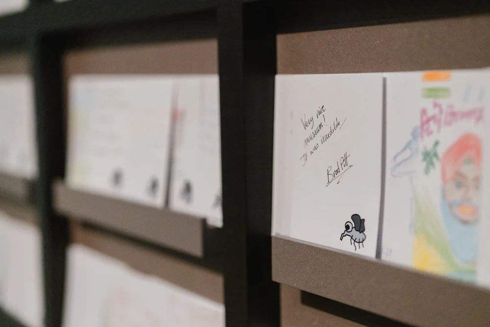 An einer Wand hängen Illustrationen und handschriftliche Kommentare auf quadratischen Papierblättern.