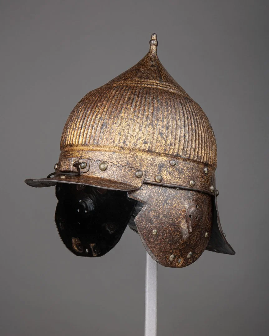 Auf dem Foto ist ein Vergleichsobjekt aus dem mitteleuropäischen Raum zu sehen. Es handelt sich ebenfalls um einen metallenen Helm mit Augenschirm in "orientalisierender" Form.