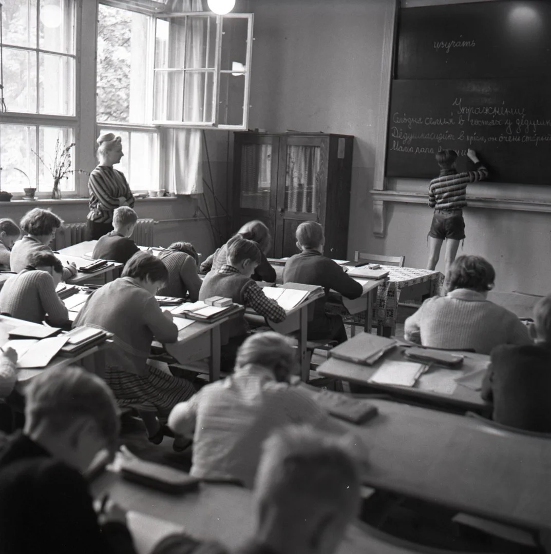 Die „Verdiente Lehrerin des Volks“ Elisabeth Urban der 13. POS Berlin-Mitte erteilt Russischunterricht, 1962 © Martin Schmidt / DHM Schwarz-weiß Fotografie mit Kindern in einem Klassenzimmer, Blick auf die Tafel auf der die Lehrerin schreibt