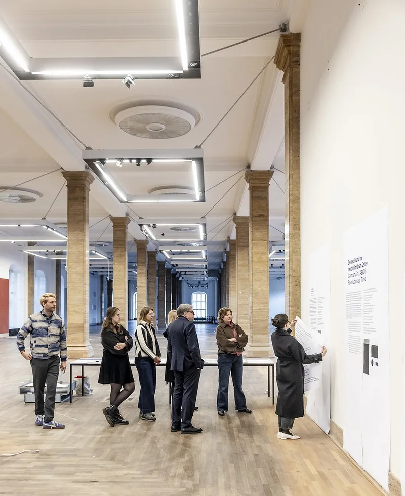 A group of people are looking at printouts in different font sizes that have been put up on a wall in the armoury.