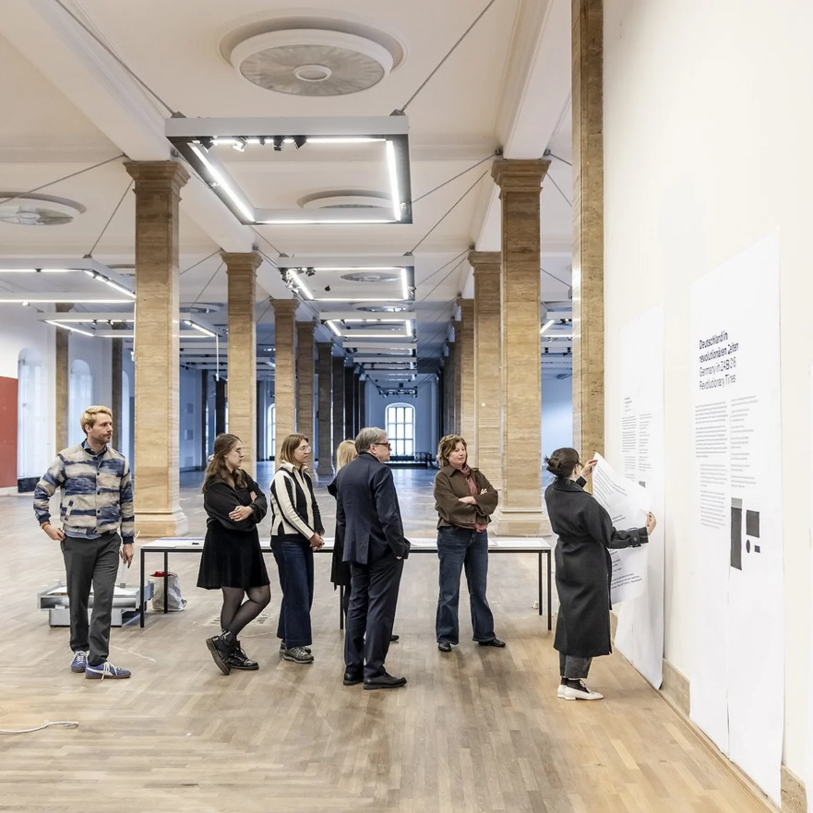 A group of people are looking at printouts in different font sizes that have been put up on a wall in the armoury.
