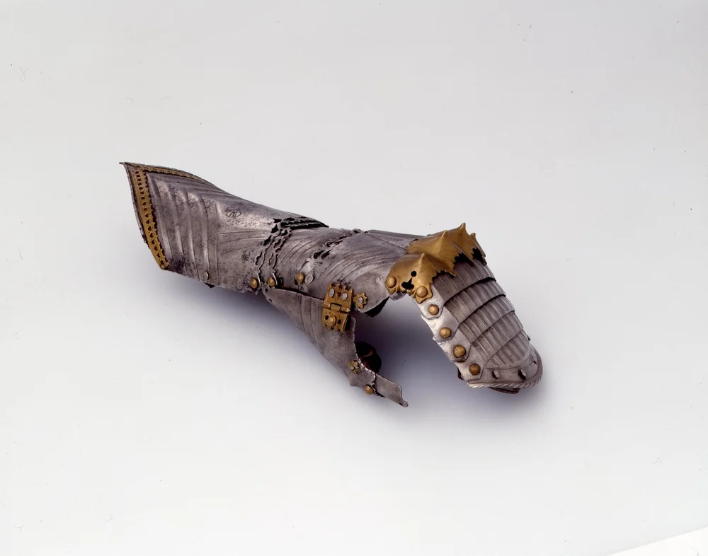 Das Bild zeigt einen metallenen Panzerhandschuh der linken Hand, der auf einem weißen Untergrund liegt.