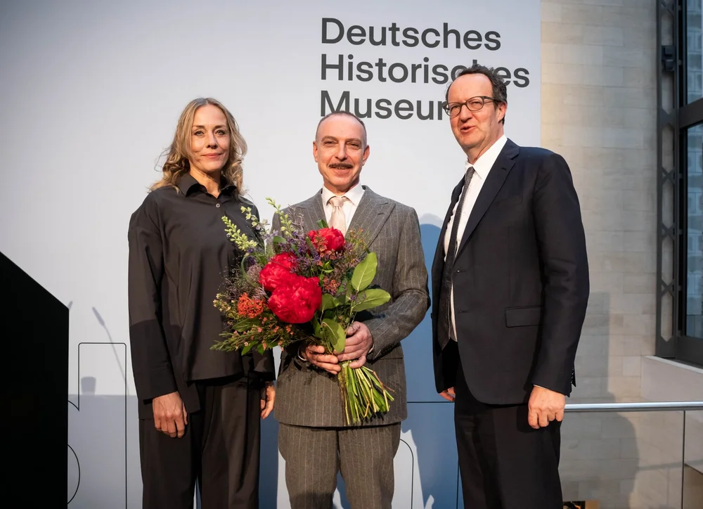 Zu sehen sind Charlotte Klonk, Wolfgang Cortjaens mit einem Blumenstrauß und DHM-Raphael Gross nach den von ihnen gehaltenen Reden.