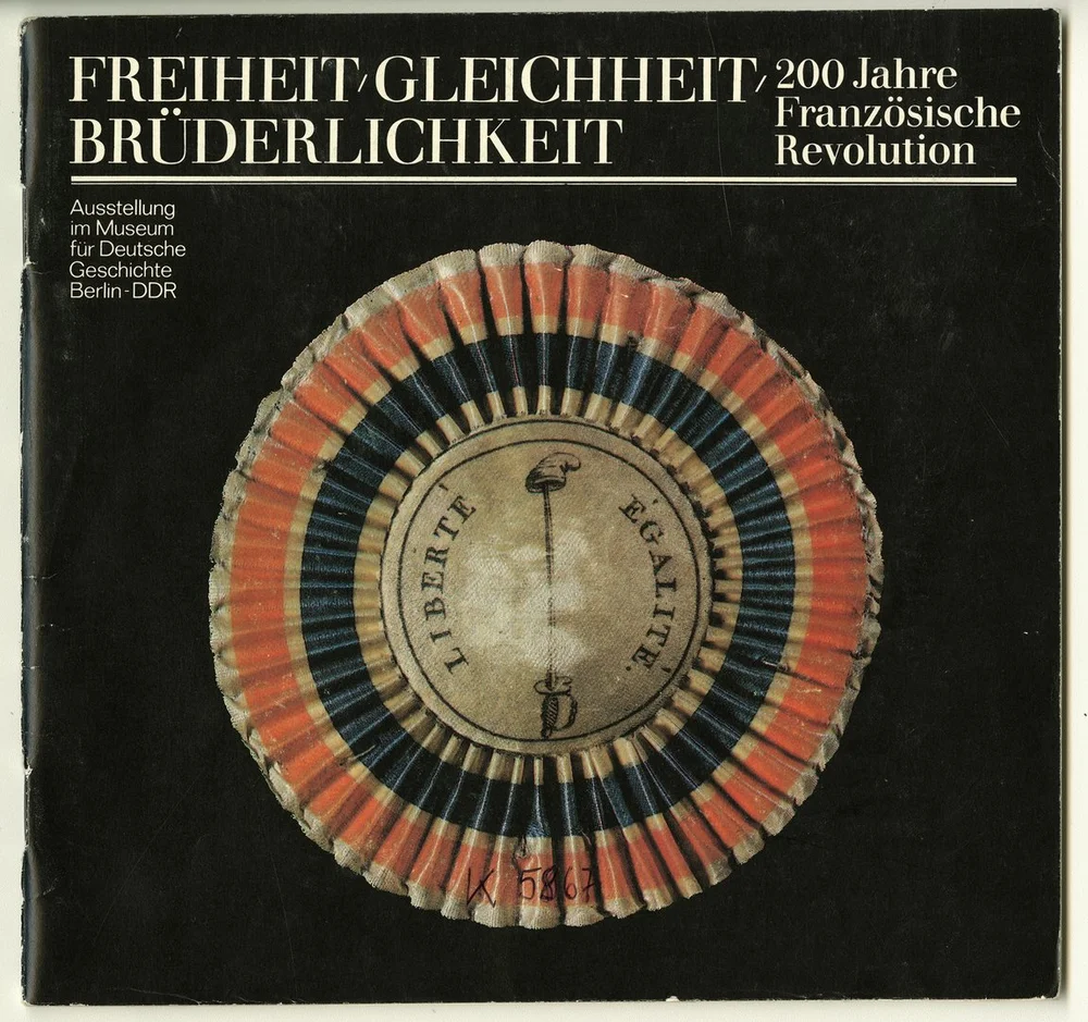 Auf dem Foto ist die Broschüre der zur Ausstellung „Freiheit, Gleichheit, Brüderlichkeit. 200 Jahre Französische Revolution.“ abgebildet. Auf dem schwarzen Hintergrund ist die Tricolore mit den Wirten „Liberté“ und „Égalité“ zu lesen.