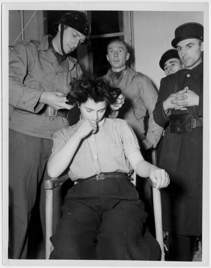 The picture shows four French soldiers cutting the hair of a female collaborator, who is sitting on a chair in the centre of the picture.