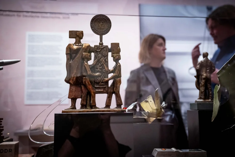 Ausstellungsansicht von „Objekte. Geschichte. Geschichten.“ mit Blick in eine Vitrine, im Hintergrund sind Besucherinnen und Besucher zu erkennen.
