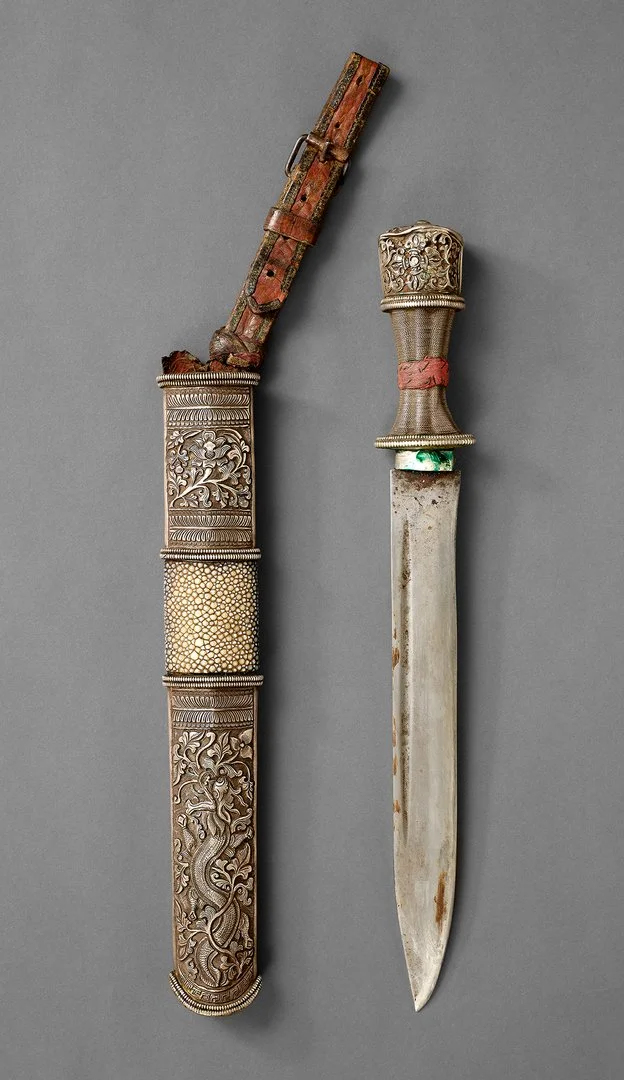 Das Foto zeigt einen tibetanischen Dughti, d.h. ein kulturell bedeutsamer Dolch mit breiter Klinge und verziertem Griff. Darunter liegt die ebenso reichverzierte Dolchscheide.