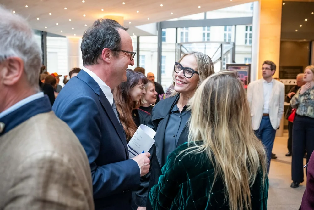Personen, die im Foyer des Pei-Baus zur Eröffnung der Ausstellung „Objekte. Geschichte. Geschichten.“ stehen und sich unterhalten.