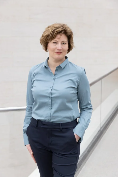 [Translate to English:] Portraitfoto von Stephanie Neuner. Sie hat kurze blonde Haare, trägt ein blaues Hemd und eine schwarze Hose. 