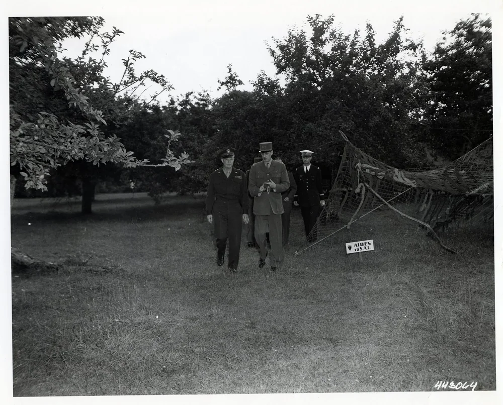 Black-and-white photograph: Eisenhower and de Gaulle walking across a meadow.