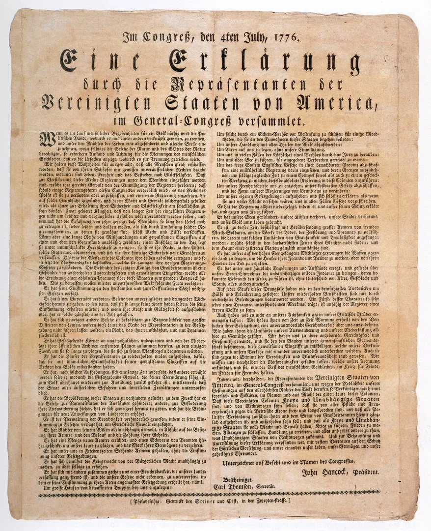 Historisches Druckdokument auf vergilbtem Papier. Überschrift in Frakturschrift: „Im Congreß, den 4ten July, 1776. Eine Erklärung durch die Repräsentanten der Vereinigten Staaten von America, im General-Congreß versammlet.“ Darunter engbedruckter Fließtext in zwei Spalten, am unteren Rand Unterschriften, darunter „John Hancock, Präsident“. Das Papier zeigt deutliche Alterungsspuren mit leichter Bräunung und unregelmäßigen Rändern.