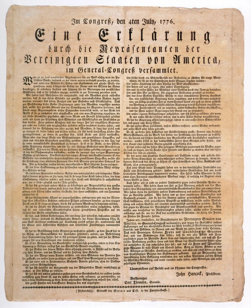 Historisches Druckdokument auf vergilbtem Papier. Überschrift in Frakturschrift: „Im Congreß, den 4ten July, 1776. Eine Erklärung durch die Repräsentanten der Vereinigten Staaten von America, im General-Congreß versammlet.“ Darunter engbedruckter Fließtext in zwei Spalten, am unteren Rand Unterschriften, darunter „John Hancock, Präsident“. Das Papier zeigt deutliche Alterungsspuren mit leichter Bräunung und unregelmäßigen Rändern.